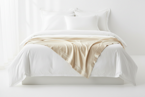 Bed with white bedding and a beige blanket on a white background